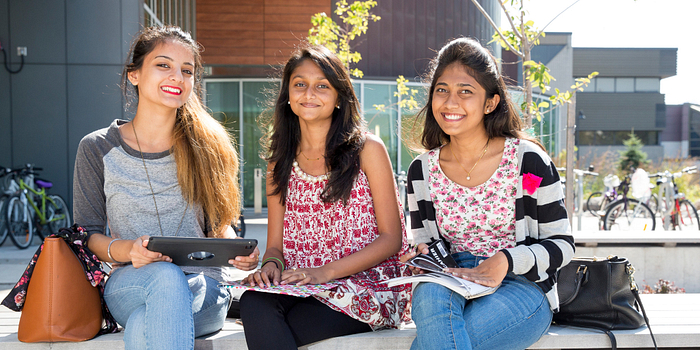 picture of three centennial college students sitting outside progress campus on a bench
